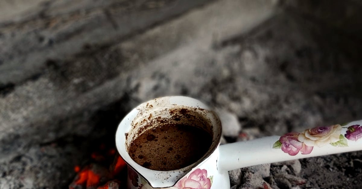 Close-up of a floral cezve brewing coffee on hot coals in a traditional setting.